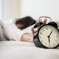 mujer sonolienta alcanzando sosteniendo despertador rutina ¿Cómo volver a la rutina después del aislamiento?